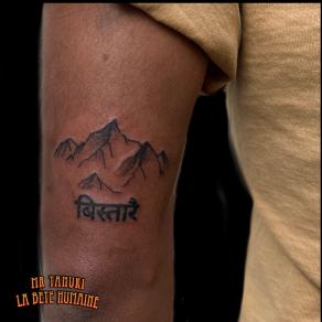 Peter Galt, tatoueur à Paris - Chaîne montagneuse et lettrage tatoués derrière le biceps